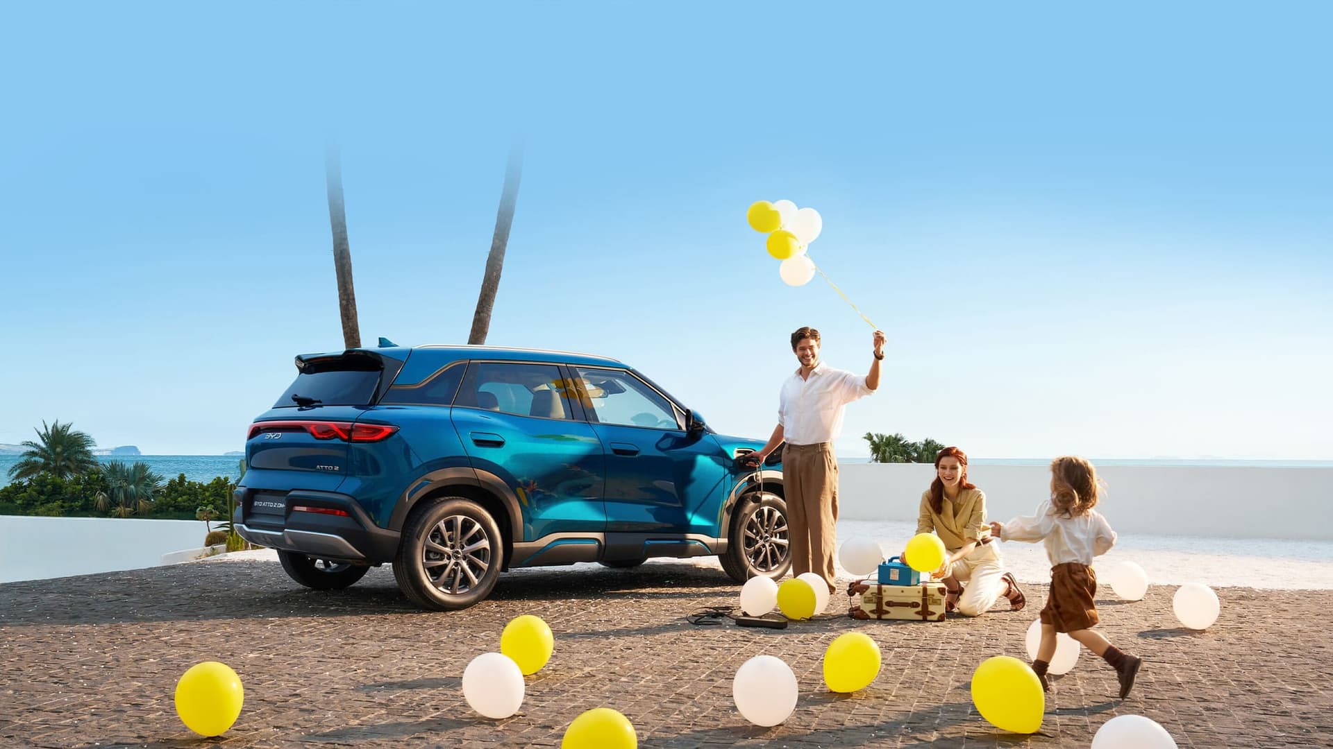 Familia con globos junto a un BYD Atto 2 DM-i azul frente al mar